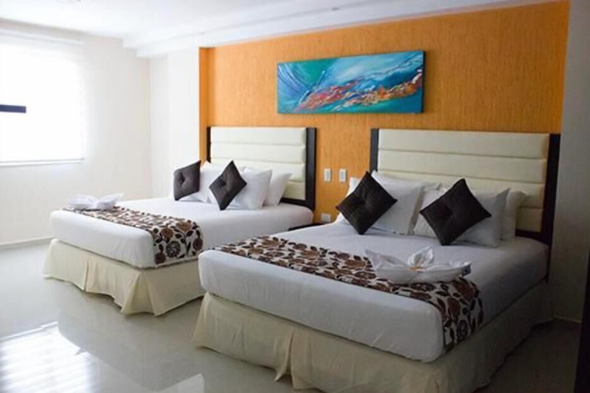 Una habitación de hotel con dos camas, cada una con cabecera, ropa de cama blanca y un cojín decorativo.