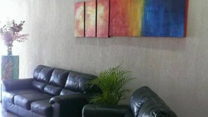 Un hall d’entr ée avec deux canapés en cuir noir, une grande peinture abstraite et une plante en pot.
