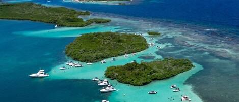 An aerial view of a tropical island with clear turquoise waters, surrounded by smaller islands and a clear sky.