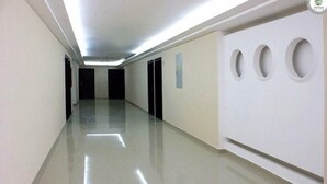 Un long couloir étroit doté d’un sol brillant, de portes noires et d’un mur blanc orné d’ouvertures circulaires.