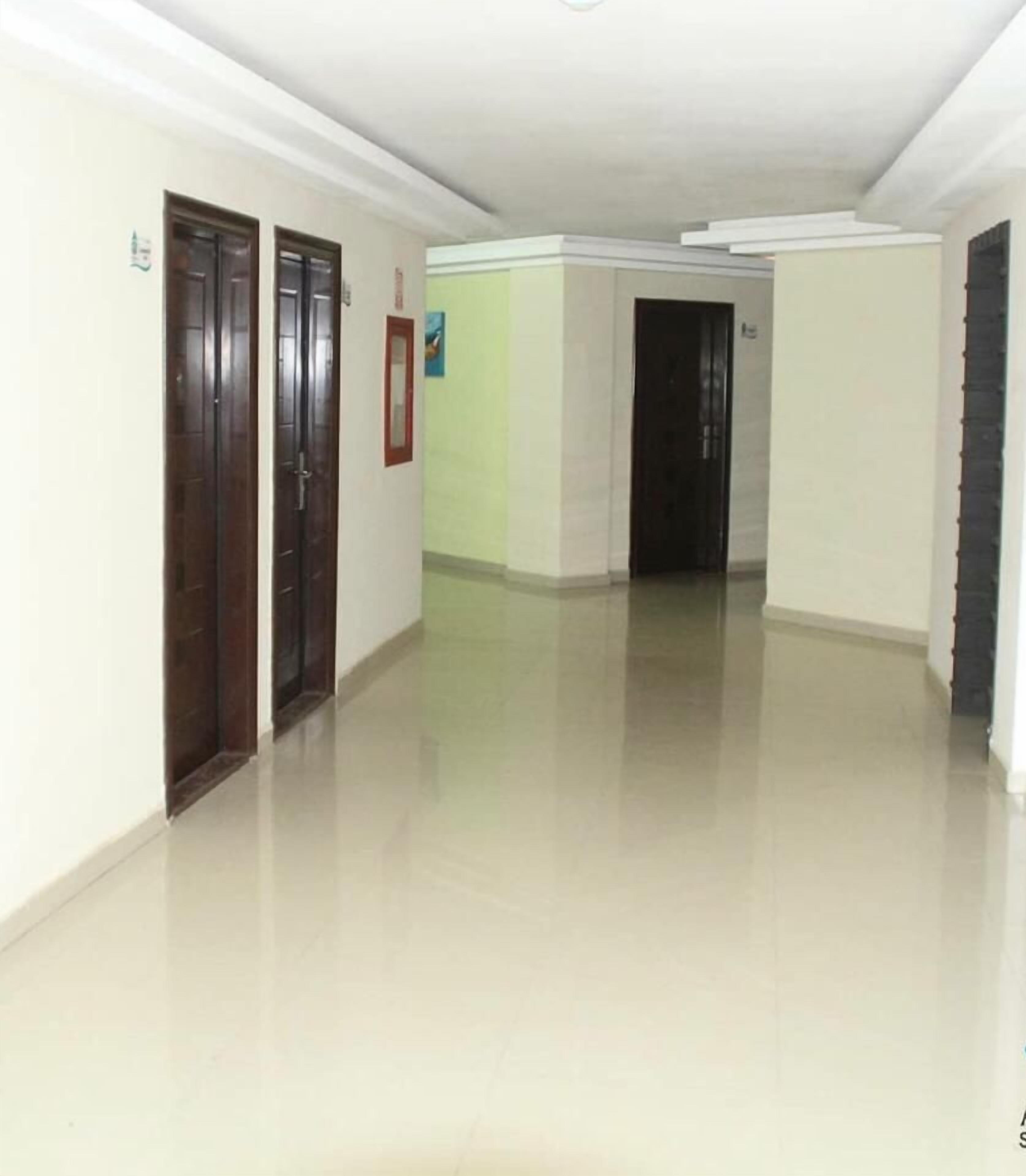Un pasillo con dos puertas de madera, piso de color claro y pared blanca con un pequeño cuadro enmarcado.