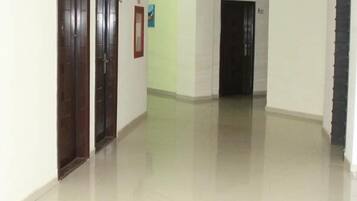 Un pasillo con dos puertas de madera, piso de color claro y pared blanca con un pequeño cuadro enmarcado.