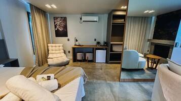 A modern hotel room with a bed, a sofa, a desk, a chair, and a small table. There is a wardrobe and a fireplace.