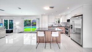 Une cuisine moderne dotée d’un îlot central, d’appareils électroménagers en acier inoxydable et offrant une vue sur un jardin luxuriant.
