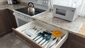 Una cocina con un cajón que contiene varios utensilios y una tetera sobre la hornilla.