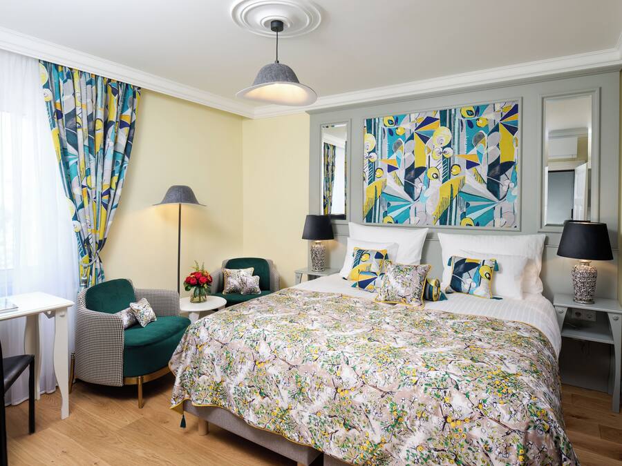 A hotel room with a large bed, a desk, a chair, and a small table.