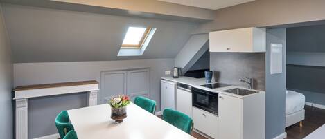 A compact kitchen with a dining area, a skylight, and a bed in the adjacent room.