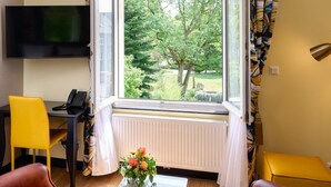 A room with a large window, a desk with a telephone, a TV mounted on the wall, and two leather chairs. - Hotel The Rose by Goeres (Luxembourg City)