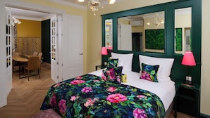 A bedroom with a floral bedspread, a large mirror, and two bedside lamps. - Hotel The Rose by Goeres (Luxembourg City)
