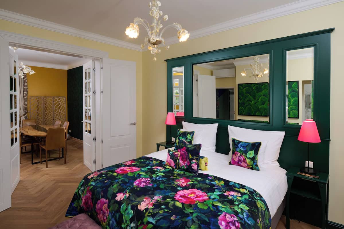Un dormitorio con una colcha estampada, un espejo grande y dos lámparas de noche.
