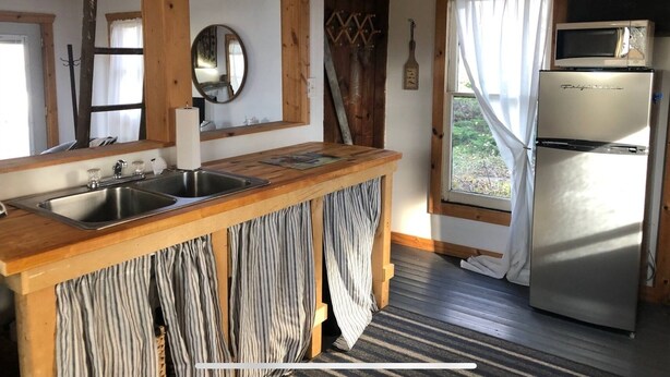 Eine rustikale Küche mit Holzbalken, einem Spülbecken, einem Kühlschrank und einem Fenster mit Vorhängen.
