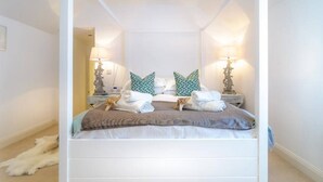 A four-poster bed with white bedding, two nightstands with lamps, and decorative pillows. - The Cove, Porthtowan (Porthtowan)