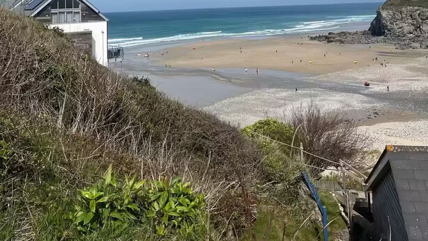 A coastal view with a beach, a building with a garage, and a rocky cliff. - The Cove, Porthtowan (Porthtowan)