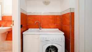 A compact laundry room with a washing machine, a sink, and orange-tiled walls. - BARIROOMS - PICCINNI (Bari)