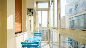 A balcony with a table and chairs, a window with blinds, and a view of buildings. - BARIROOMS - PICCINNI (Bari)