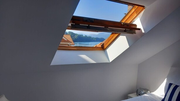 A bedroom with a skylight, a bed, a bedside table, and a chair.