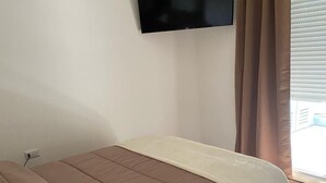 Une chambre à coucher avec un lit, un téléviseur fixé au mur, une lampe sur une table de chevet et une fenêtre avec des rideaux.