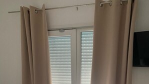Une pièce avec une table et une chaise blanches, des rideaux beiges et une porte-fenêtre coulissante donnant sur un espace extérieur.