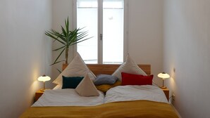 A bedroom with a bed, two bedside lamps, a chandelier, a window, and a potted plant. - Apartment in the middle of a wine paradise (Rhodt unter Rietburg)