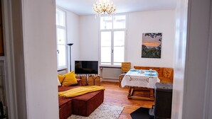 A cozy living room with a sofa, a television, a dining table with chairs, and a chandelier. - Apartment in the middle of a wine paradise (Rhodt unter Rietburg)