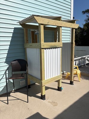 Une cabane en bois pour enfants, avec un côté en métal ondulé, une chaise et un tabouret jaune.