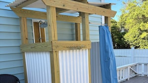 A wooden pergola structure with a metal roof, a white vertical panel, and a blue curtain.