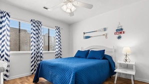 A bedroom with a bed, a nightstand, a lamp, a ceiling fan, and nautical-themed wall decorations.