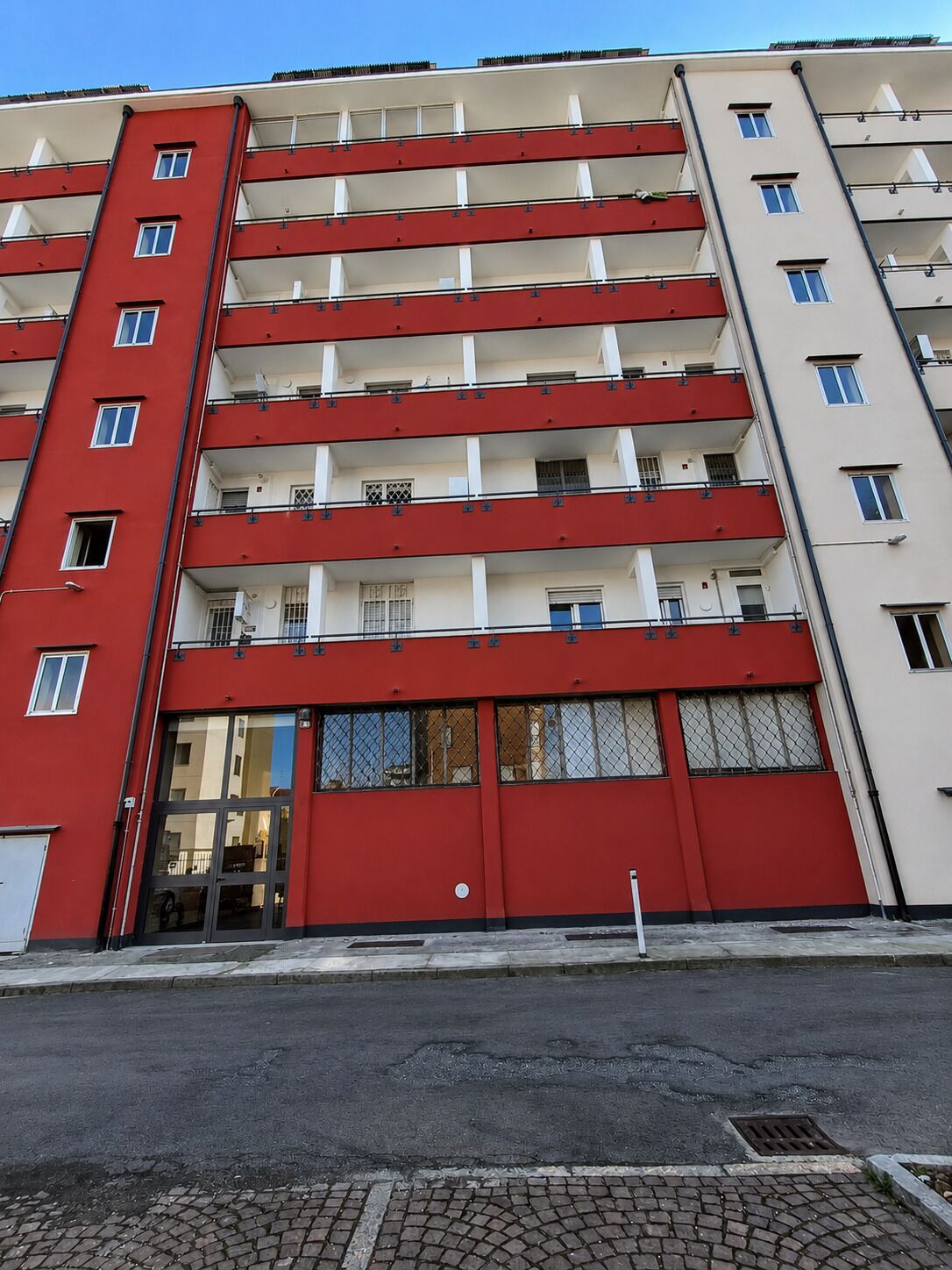 A multi-story building with balconies, a red door, and a clear sky.