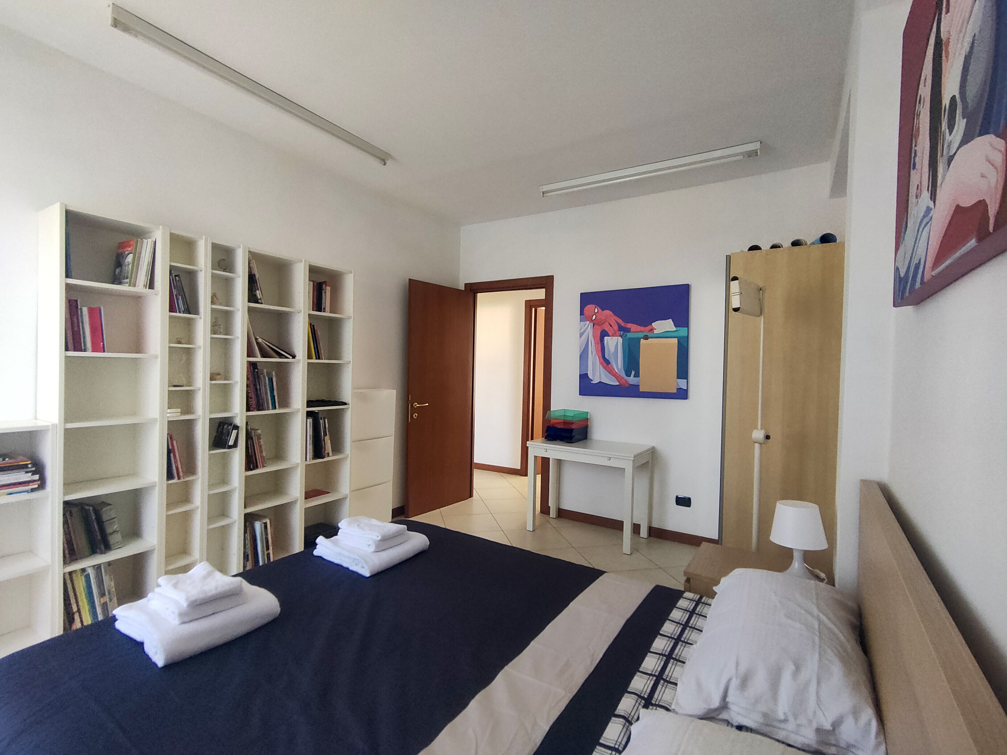 Un dormitorio con una cama grande, una estantería, un escritorio y una puerta que da a otra habitación.