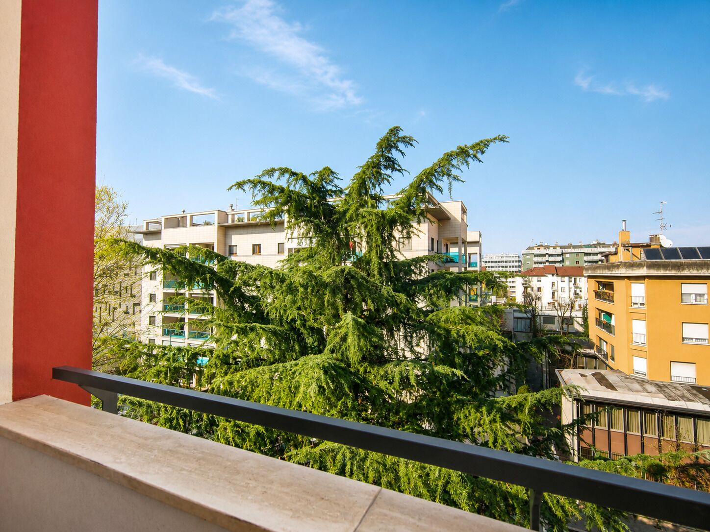 Een balkon met uitzicht op woongebouwen en bomen.