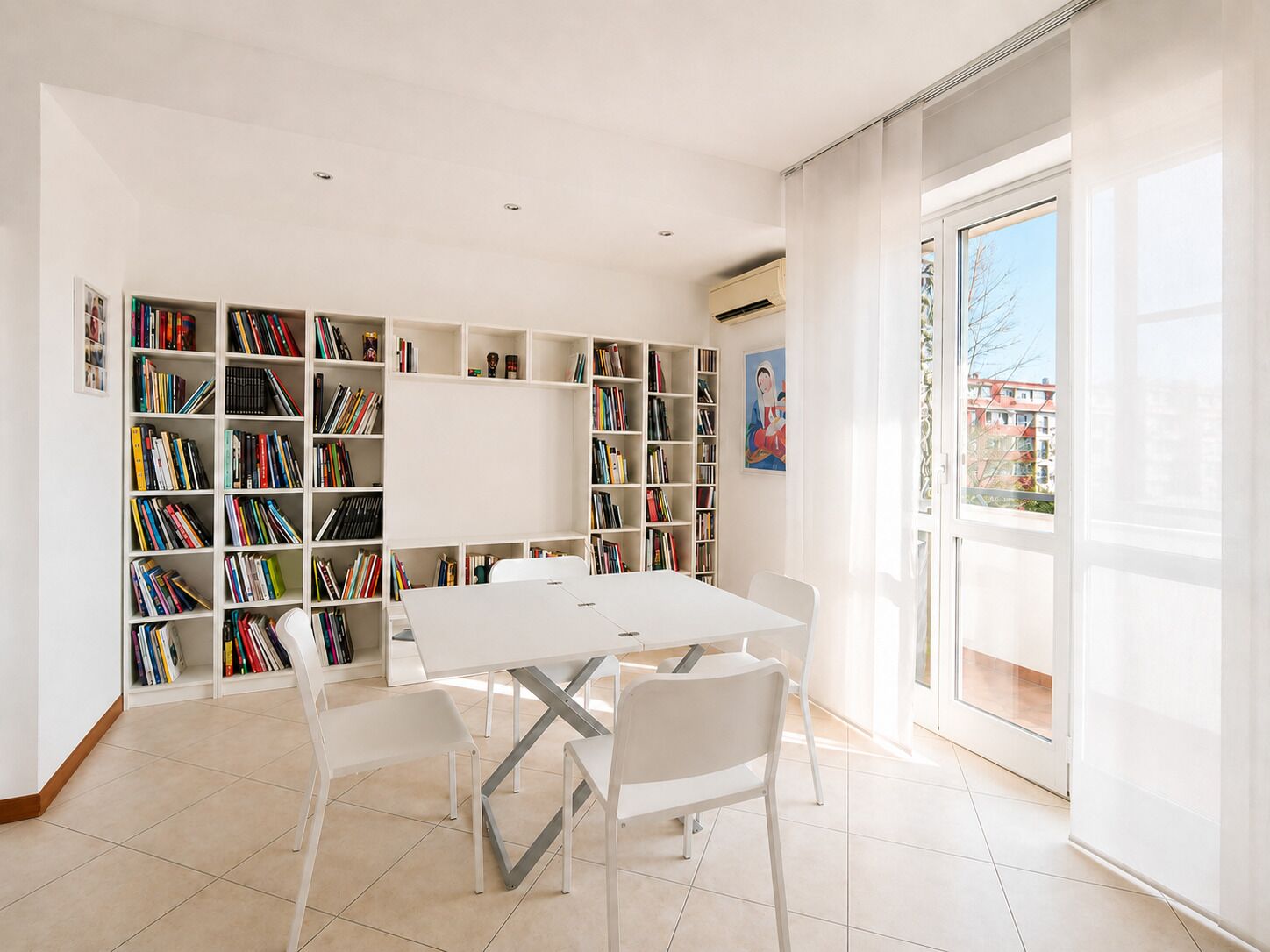 Een ruime kamer met een witte tafel en stoelen, omringd door boekenkasten vol boeken.