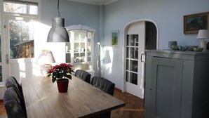 Un coin repas avec une table en bois, des chaises, une plante en pot, un luminaire suspendu et une vue sur l’extérieur par une fenêtre.