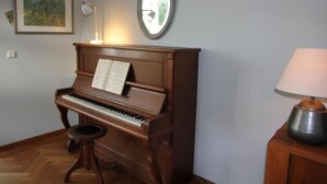 Un piano droit en bois, avec des partitions posées sur le dessus, un petit tabouret, une lampe de bureau et un miroir accroché au mur.