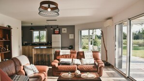 A modern living room with leather sofas, a coffee table, and a kitchen area visible through an open door. - l'Acacia, swimming pool and large garden (Bénesse-Maremne)