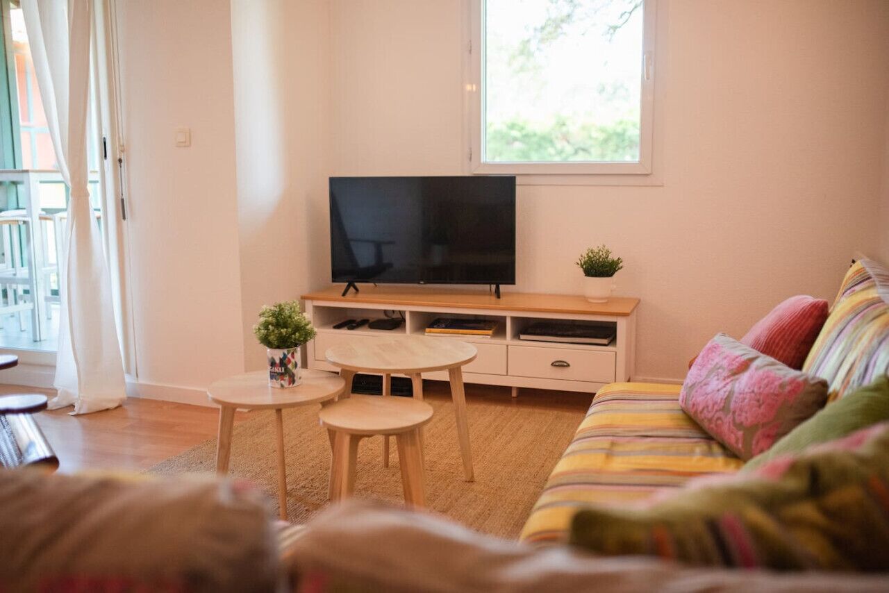 Een woonkamer met een televisie op een houten standaard, een bank, een bijzettafeltje en een plant in een pot.