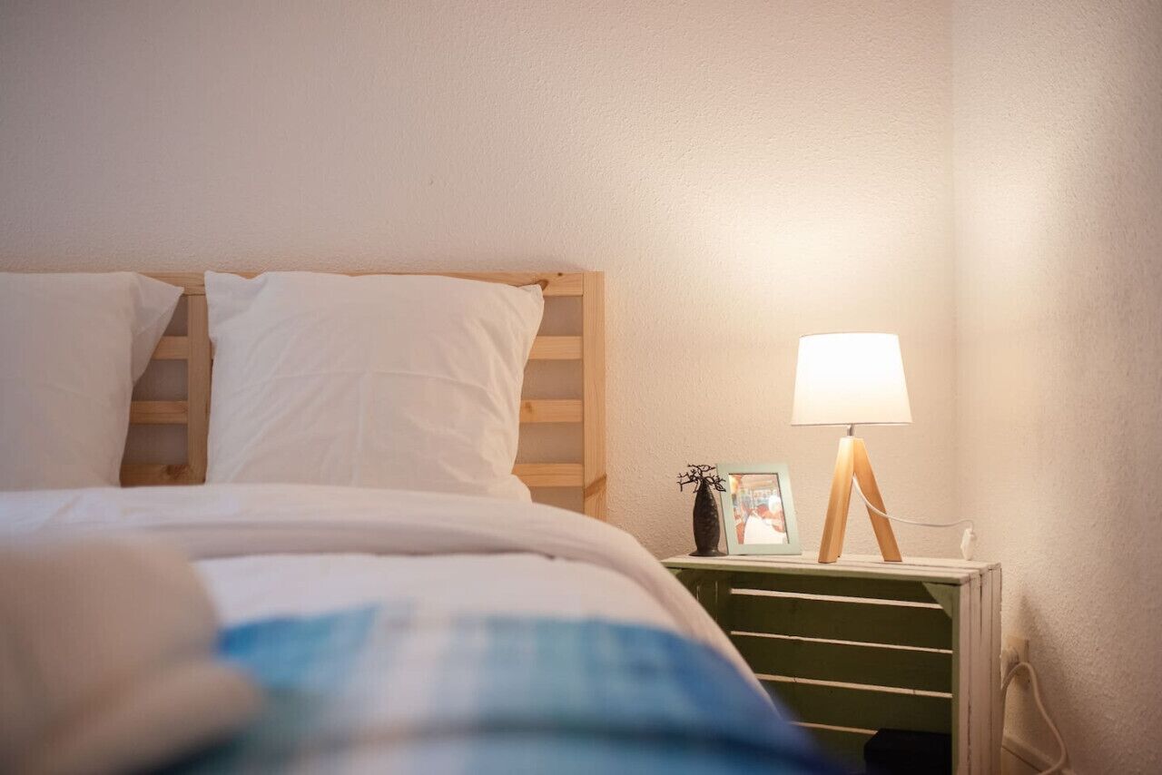 A neatly made bed with white linens, a bedside table with a lamp, and a framed picture on the table.