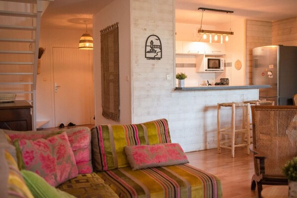 Una sala de estar acogedora con un sofá, una mesa de centro de madera y una zona de cocina con microondas y refrigerador.