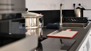 Une cuisine moderne dotée d’appareils électroménagers en acier inoxydable, d’un plan de travail noir et d’une planche à découper rouge.