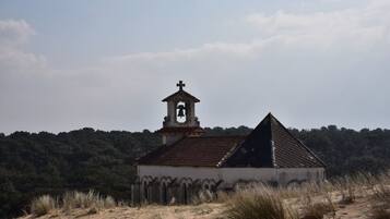 A small, isolated church with a bell tower and a triangular roof, surrounded by dry grass and trees.