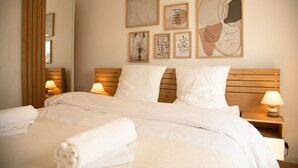 Un lit bien fait, avec du linge de lit blanc et une serviette enroulée, une tête de lit en bois, des lampes de chevet et des œuvres d’art encadrées accrochées au mur.