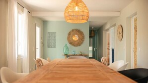 A dining area with a wooden table, white chairs, a woven pendant light, and a wall clock.
