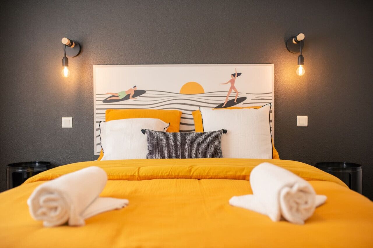 Un lit recouvert d’une couverture jaune, deux serviettes enroulées et un oreiller à motifs rayés.