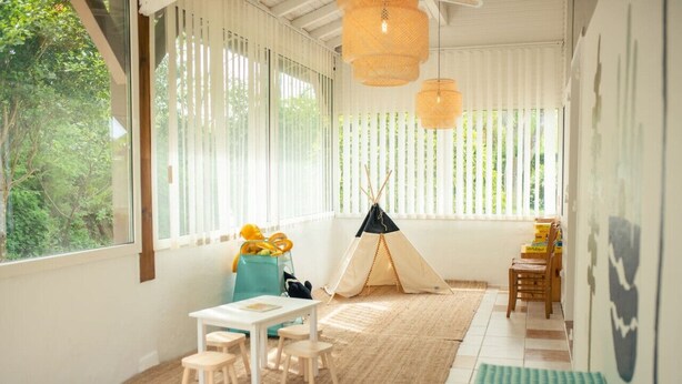 A room with a white table, chairs, a small tent, and a window with vertical blinds.