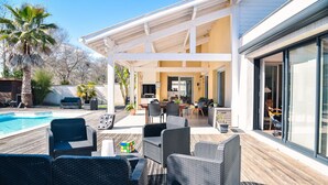 Un patio moderno al aire libre con mobiliario de mimbre, una piscina y una zona de estar cubierta.