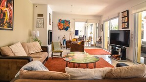 Una sala de estar con un sofá, sillones, una mesa de centro y un televisor. Hay un cuadro en la pared y una ventana con vistas.