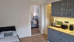 Een slaapkamer met een bed, nachtkastje en een klein kitchenette met kastjes en aanrecht.