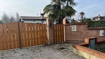 Ein von einer Hecke umgebener Garten mit Kiesboden, eine Ziegelmauer mit Briefkasten und eine Palmenbaum.