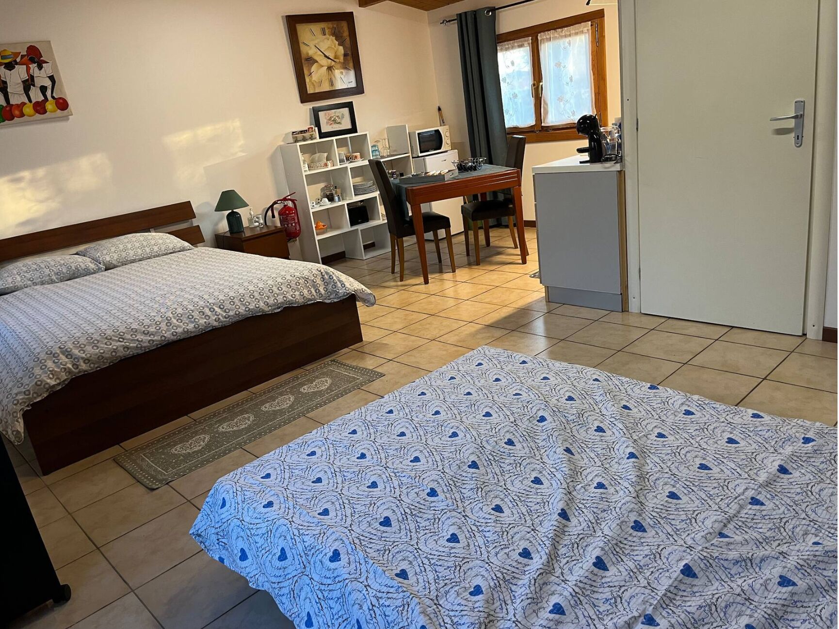 Quarto com cama, escrivaninha, cadeira, pequeno frigorífico e guarda-roupa.