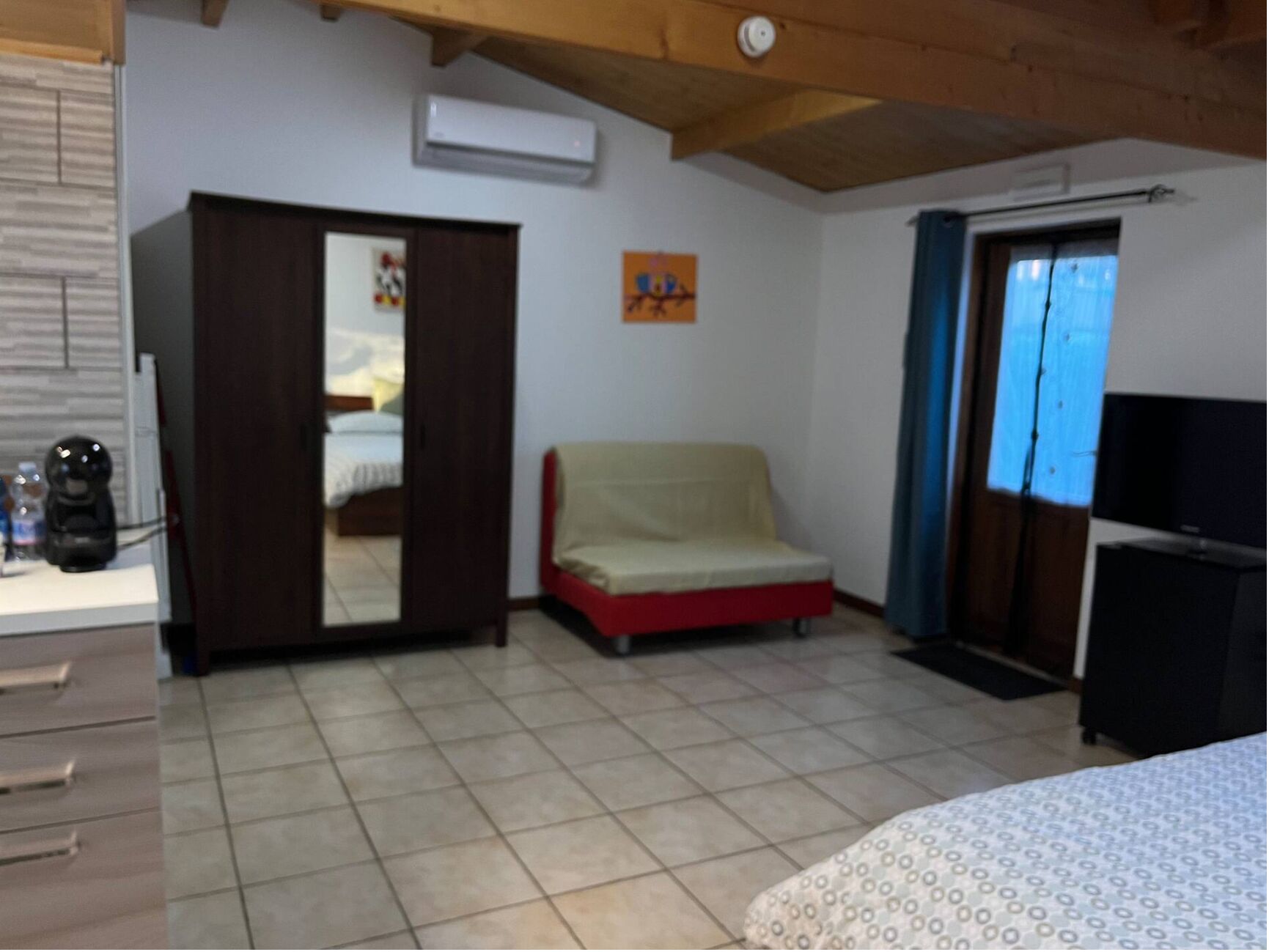 A room with a bed, a sofa, a wardrobe, a TV, and a window with curtains.