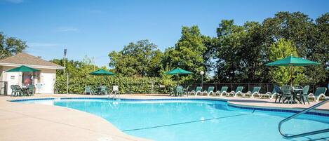 Une piscine entourée d’arbres, avec des chaises longues et des parasols.